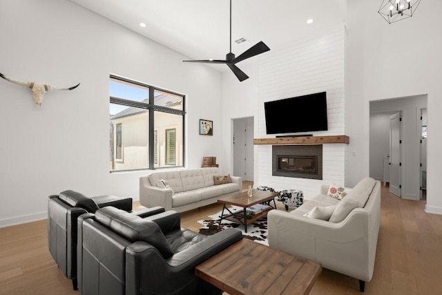 living area featuring baseboards, a high ceiling, wood finished floors, and ceiling fan with notable chandelier