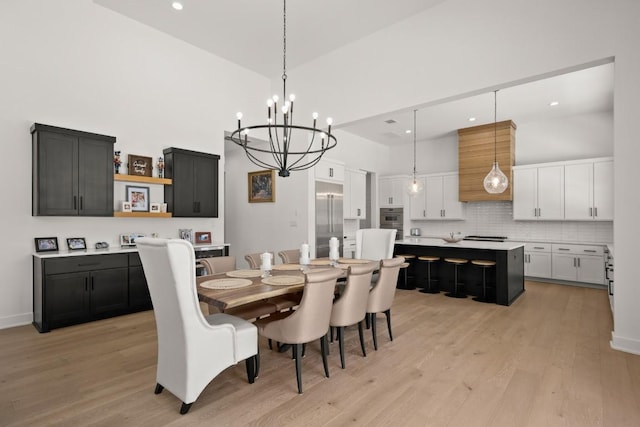 dining room featuring an inviting chandelier, recessed lighting, light wood-type flooring, and a towering ceiling