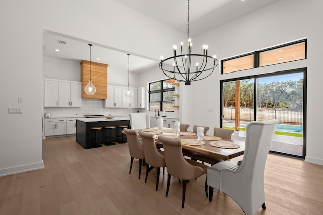 dining room featuring light wood finished floors, visible vents, baseboards, a high ceiling, and an inviting chandelier