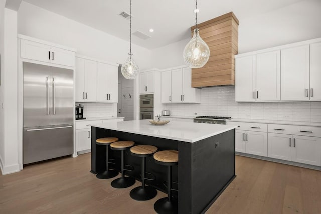 kitchen with white cabinets, wood finished floors, appliances with stainless steel finishes, and a center island