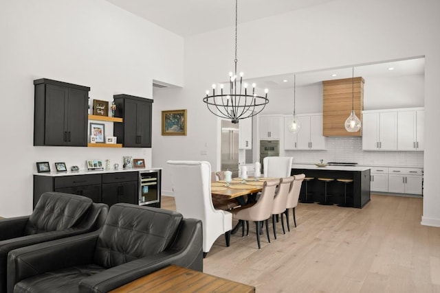 dining space featuring an inviting chandelier, beverage cooler, light wood-style floors, and a towering ceiling