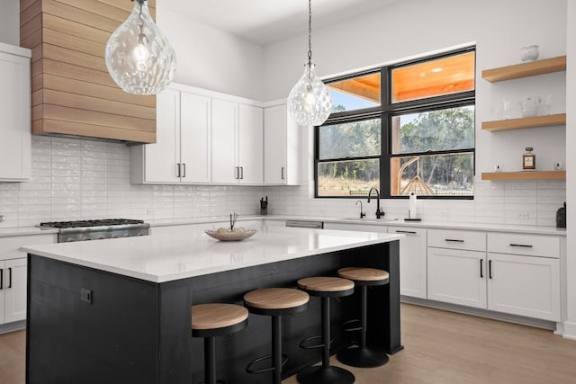 kitchen with a sink, a kitchen island, white cabinets, light countertops, and range