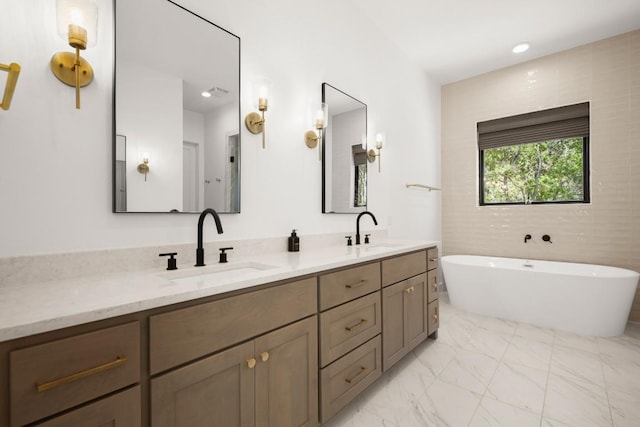 bathroom with double vanity, marble finish floor, a freestanding tub, and a sink