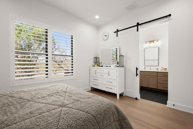 bedroom featuring a barn door, wood finished floors, visible vents, and baseboards