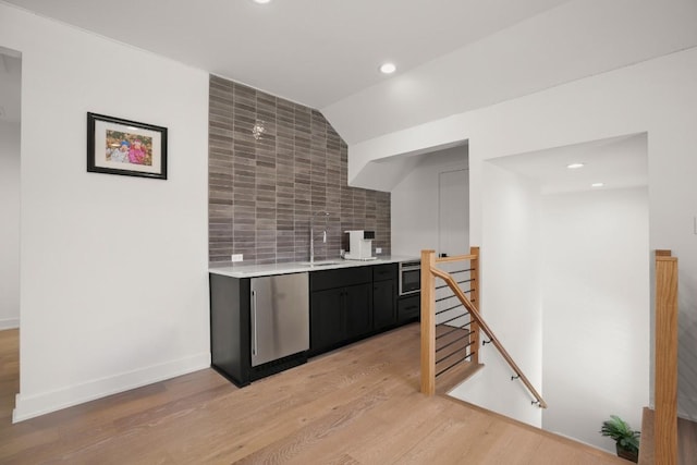 kitchen with light wood-type flooring, a sink, tasteful backsplash, light countertops, and baseboards