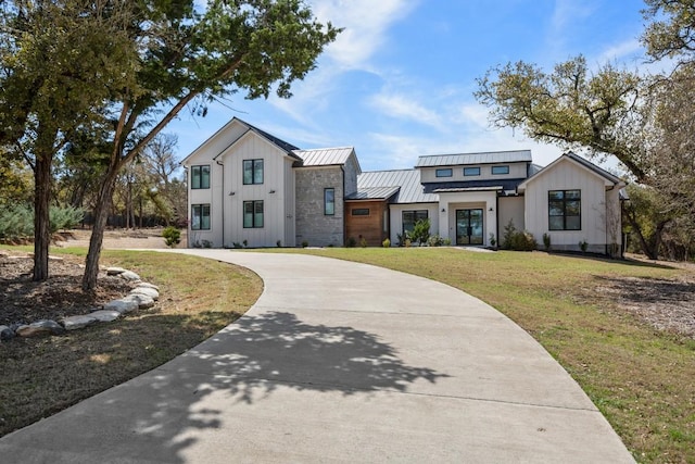 modern inspired farmhouse with board and batten siding, concrete driveway, a standing seam roof, and a front lawn