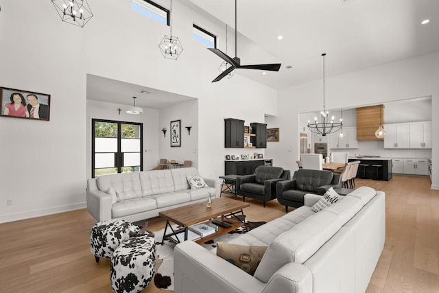 living room with light wood finished floors, baseboards, recessed lighting, ceiling fan with notable chandelier, and a high ceiling