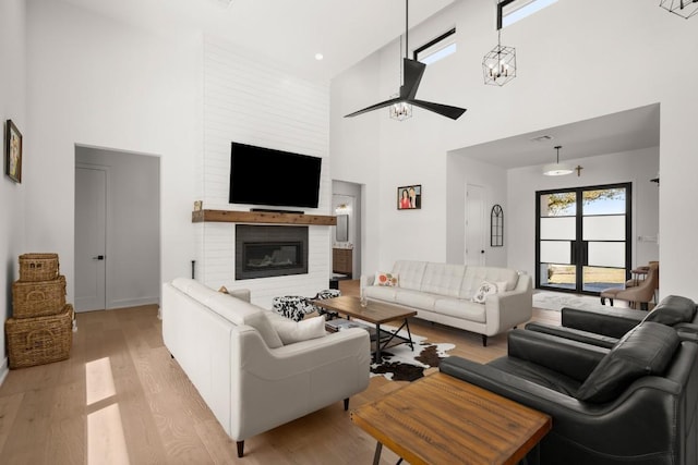 living area featuring light wood-style flooring, a fireplace, a high ceiling, and a ceiling fan