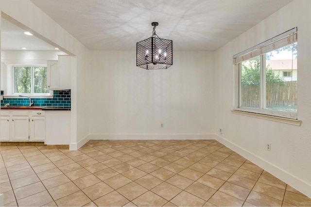 unfurnished dining area featuring an inviting chandelier, a healthy amount of sunlight, baseboards, and a sink