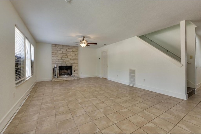 unfurnished living room featuring visible vents, baseboards, a stone fireplace, a textured ceiling, and a ceiling fan