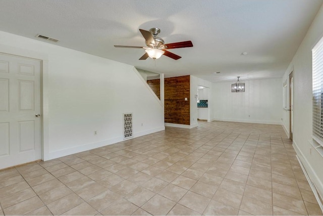 spare room featuring light tile patterned floors, visible vents, ceiling fan with notable chandelier, and baseboards