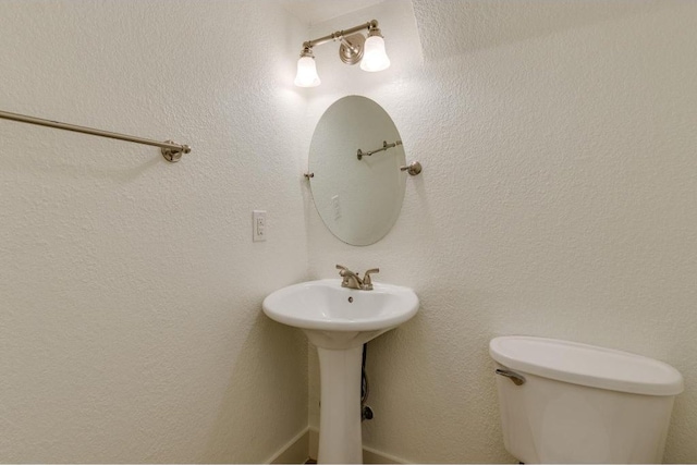 bathroom featuring a sink, toilet, and a textured wall