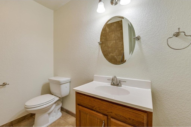 bathroom featuring baseboards, toilet, a textured wall, tile patterned floors, and vanity