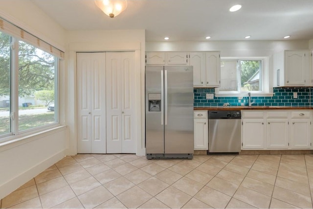 kitchen featuring light tile patterned floors, stainless steel appliances, tasteful backsplash, and white cabinets