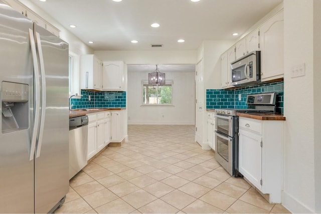 kitchen featuring light tile patterned floors, stainless steel appliances, an inviting chandelier, and white cabinetry