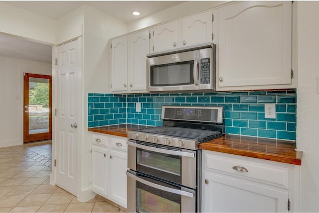 kitchen with butcher block counters, light tile patterned floors, decorative backsplash, appliances with stainless steel finishes, and white cabinets