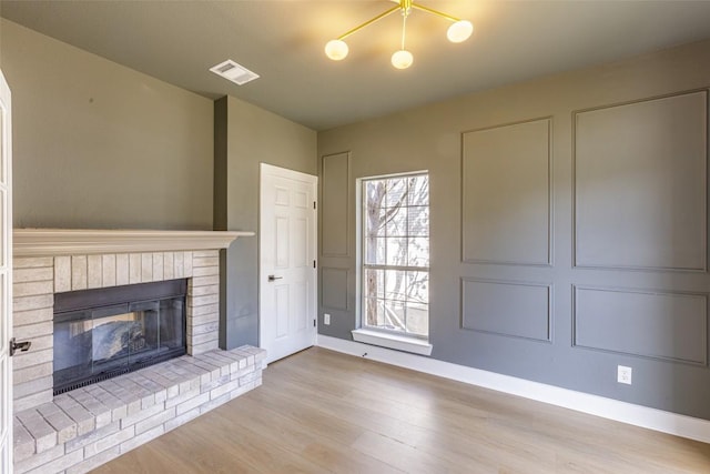 unfurnished living room with visible vents, baseboards, a fireplace, wood finished floors, and a decorative wall