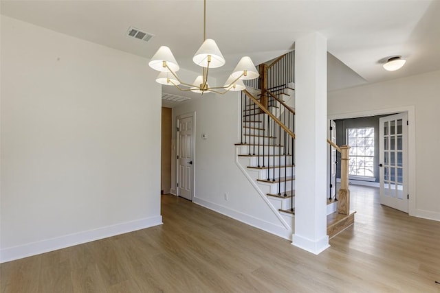 unfurnished dining area featuring visible vents, baseboards, stairs, an inviting chandelier, and wood finished floors