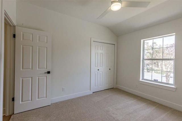 unfurnished bedroom featuring a closet, baseboards, light colored carpet, and vaulted ceiling