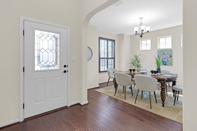 foyer entrance with dark wood-style floors, arched walkways, a wealth of natural light, and a chandelier