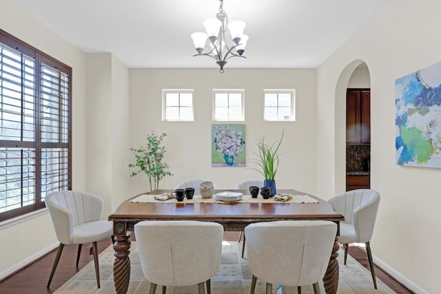 dining area with an inviting chandelier, baseboards, arched walkways, and light wood-type flooring