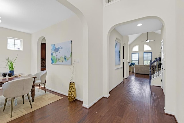 hallway featuring baseboards, arched walkways, dark wood finished floors, and stairs