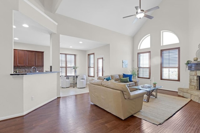 living room with high vaulted ceiling, a ceiling fan, wood finished floors, recessed lighting, and a stone fireplace