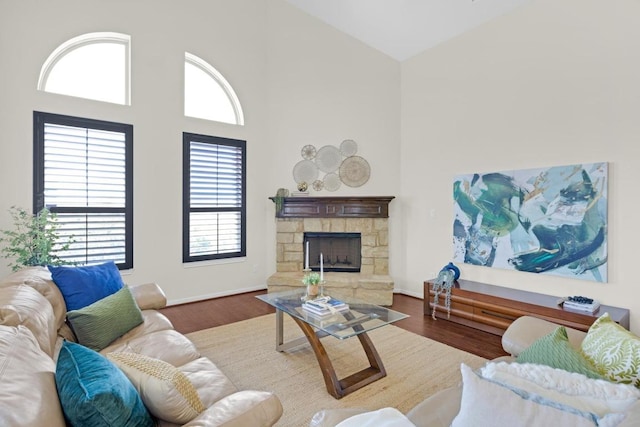 living room featuring a stone fireplace, wood finished floors, baseboards, and high vaulted ceiling