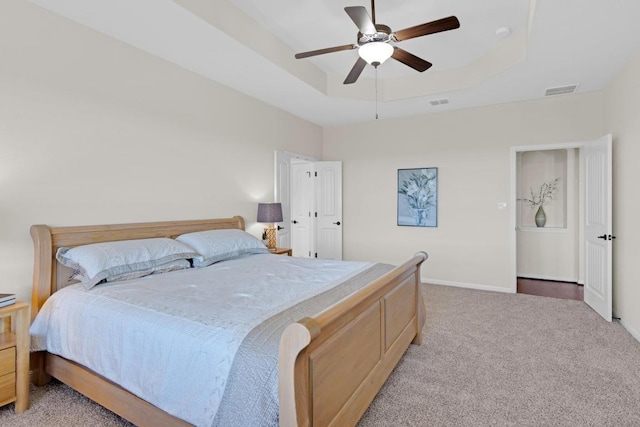 bedroom with light carpet, visible vents, a raised ceiling, and baseboards