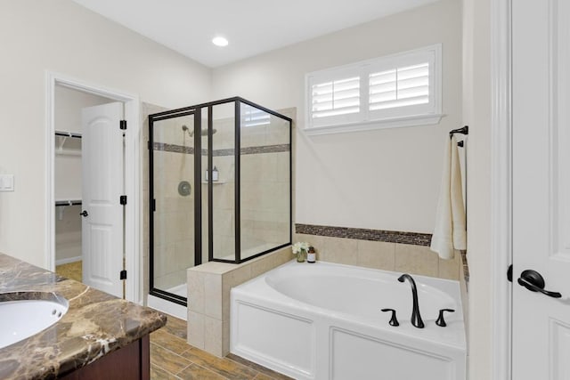 full bathroom with a walk in closet, a garden tub, recessed lighting, a stall shower, and vanity