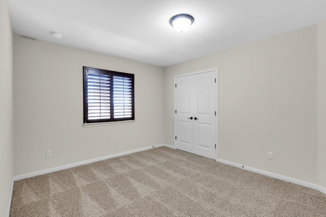 carpeted spare room featuring a textured ceiling and baseboards