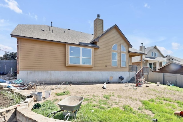 back of house featuring fence, roof with shingles, and a chimney