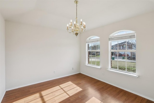 unfurnished room with an inviting chandelier, wood finished floors, and baseboards