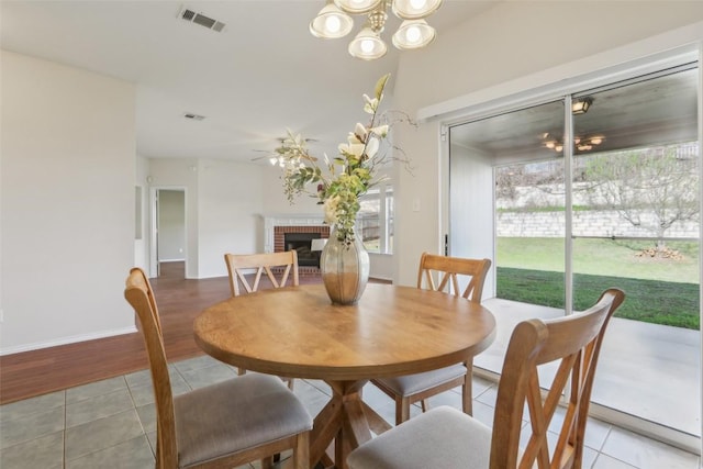 dining space featuring light tile patterned floors, visible vents, a healthy amount of sunlight, and a brick fireplace