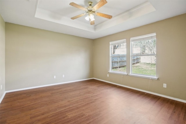 spare room with a raised ceiling, wood finished floors, and baseboards