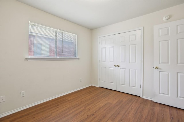 unfurnished bedroom with wood finished floors, baseboards, and a closet