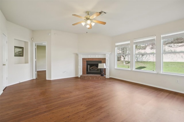 unfurnished living room with wood finished floors, a ceiling fan, visible vents, baseboards, and a brick fireplace