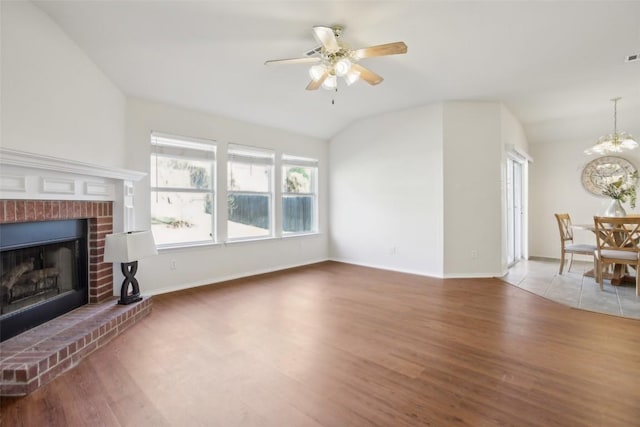 living area featuring a brick fireplace, baseboards, light wood-type flooring, vaulted ceiling, and ceiling fan with notable chandelier