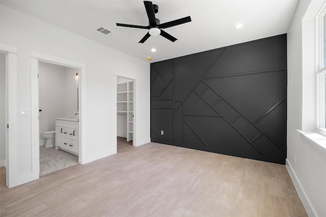 unfurnished bedroom with visible vents, a walk in closet, baseboards, an accent wall, and a closet