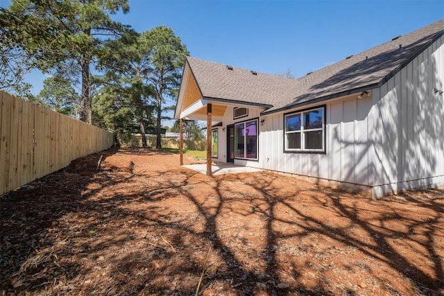 rear view of house with roof with shingles, board and batten siding, a fenced backyard, and a patio area