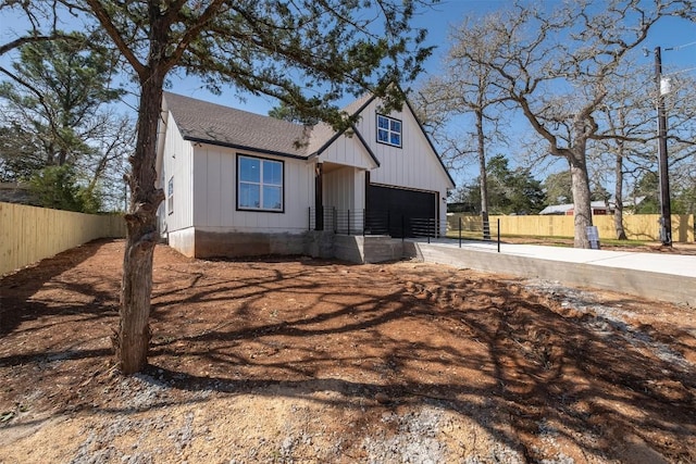 view of front facade with board and batten siding, concrete driveway, a garage, and fence