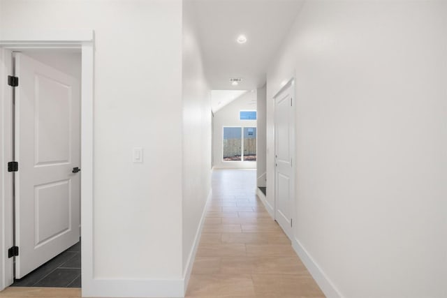 hall with light tile patterned floors, baseboards, and vaulted ceiling