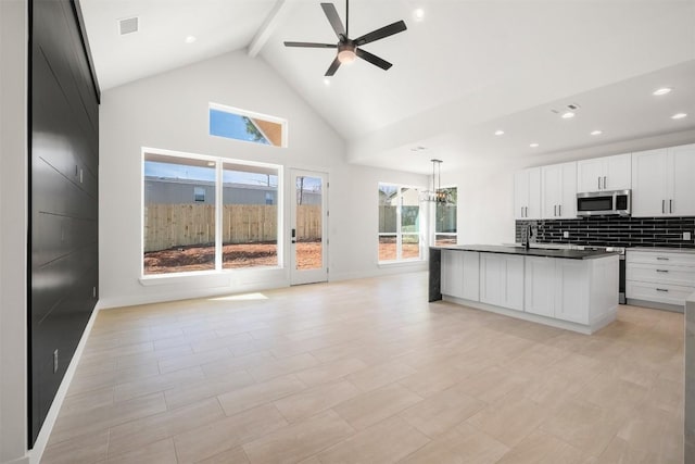 kitchen featuring dark countertops, stainless steel microwave, tasteful backsplash, open floor plan, and high vaulted ceiling