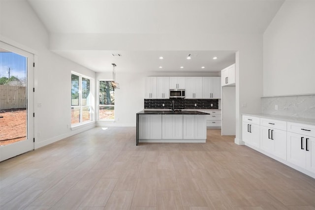 kitchen featuring stainless steel microwave, dark countertops, white cabinetry, decorative backsplash, and baseboards