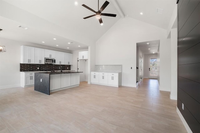 kitchen with dark countertops, decorative backsplash, stainless steel microwave, ceiling fan with notable chandelier, and open floor plan