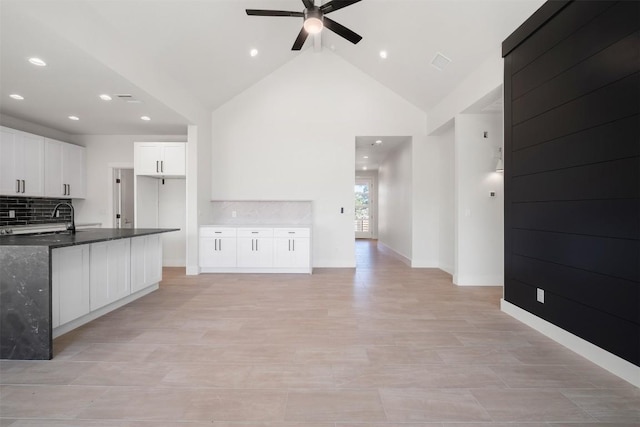 kitchen with white cabinetry, ceiling fan, decorative backsplash, high vaulted ceiling, and a sink