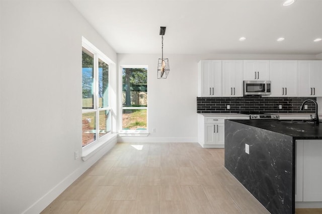 kitchen with stainless steel microwave, baseboards, decorative backsplash, white cabinetry, and a sink