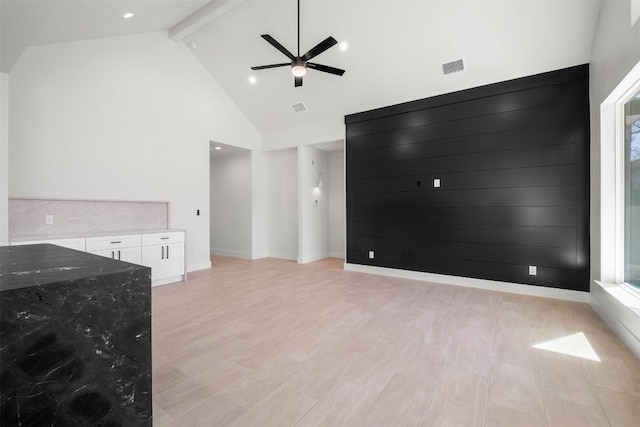 unfurnished living room with a ceiling fan, visible vents, high vaulted ceiling, beam ceiling, and light wood-style floors