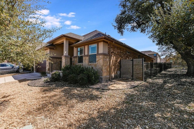 view of side of home featuring fence, concrete driveway, stucco siding, stone siding, and a gate