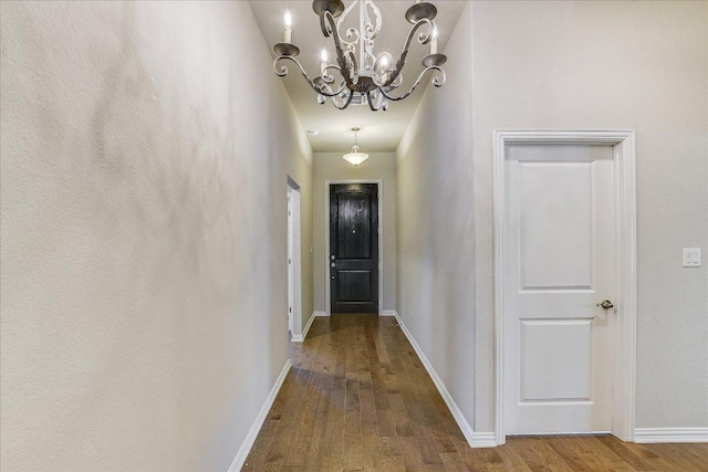 hall with an inviting chandelier, wood finished floors, and baseboards